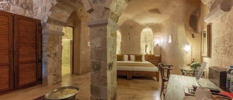Una habitación con paredes de piedra, una cama, una mesa con un ordenador portátil y un comedor con mesa y sillas.