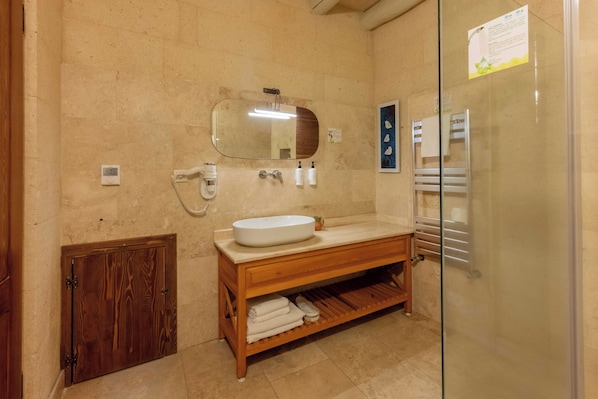 Une salle de bain avec un meuble-lavabo en bois, un lavabo blanc, un miroir, un porte-serviettes et un espace douche.