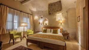 A bedroom with a large bed, two chairs, a nightstand, and wall-mounted lamps. - Peristyle Cave Cappadocia - Special Class (Nevsehir)