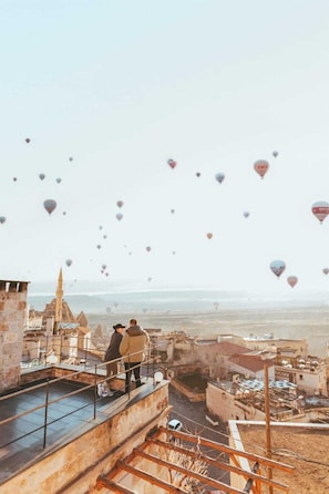 A view of a cityscape with hot air balloons in the sky and a couple standing on a rooftop. - Peristyle Cave Cappadocia - Special Class (Nevsehir)