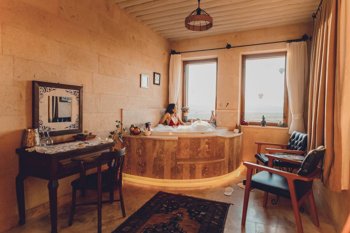Ein Zimmer mit einer Holzwanne, einem Holztisch, Stühlen und Meerblick durch zwei Fenster.