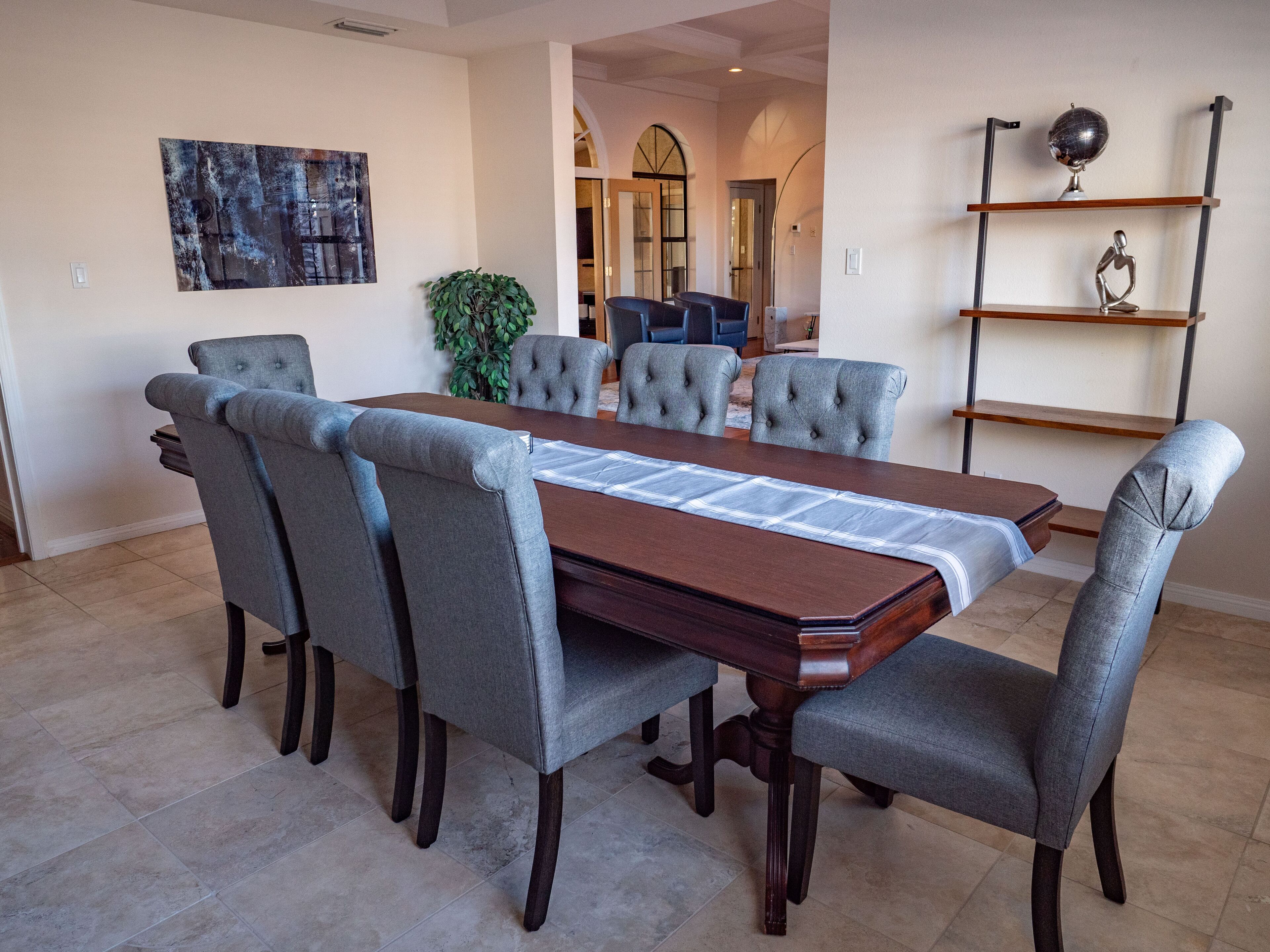 A dining area with a rectangular table, six upholstered chairs, a potted plant, and a globe on a shelf.