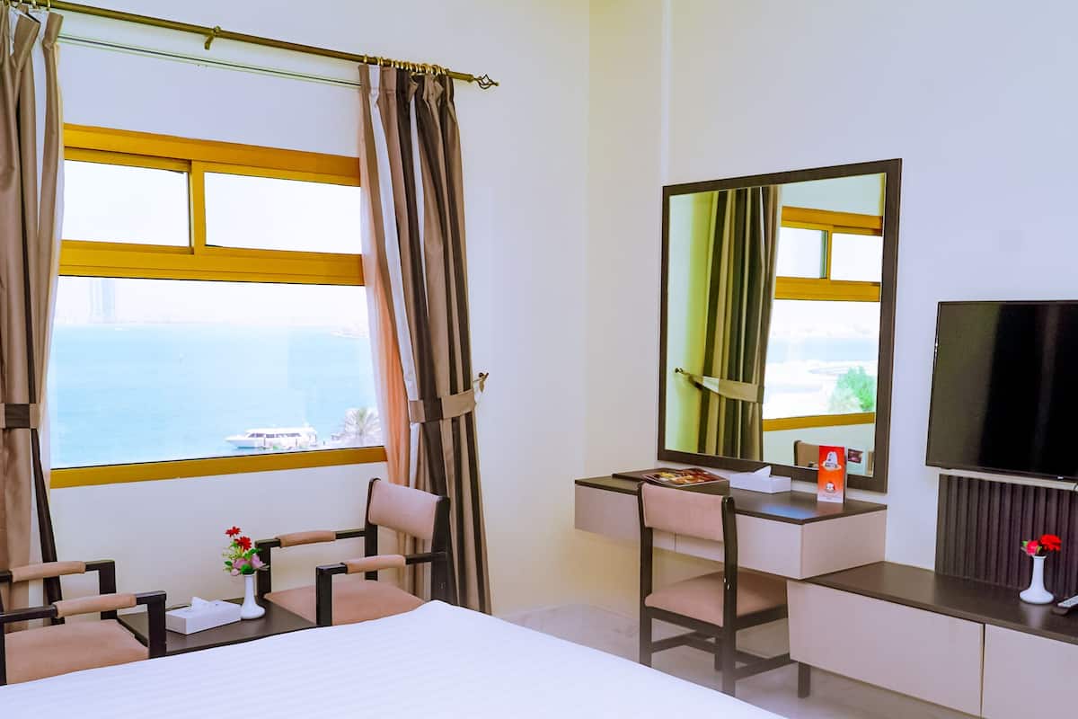 Een hotelkamer met een bed, bureau, stoel, televisie en een raam met gordijnen.