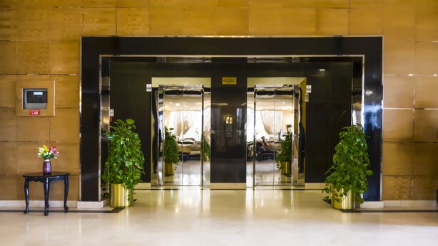 En hotelindgang med glasdør, receptionsdisk og plantekasser.