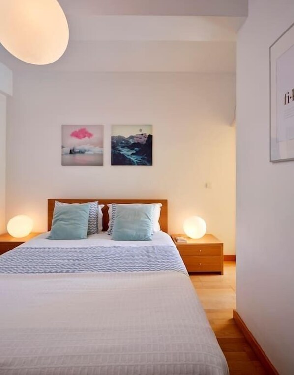 A bedroom with a large bed, two bedside tables with lamps, and two wall-mounted paintings.