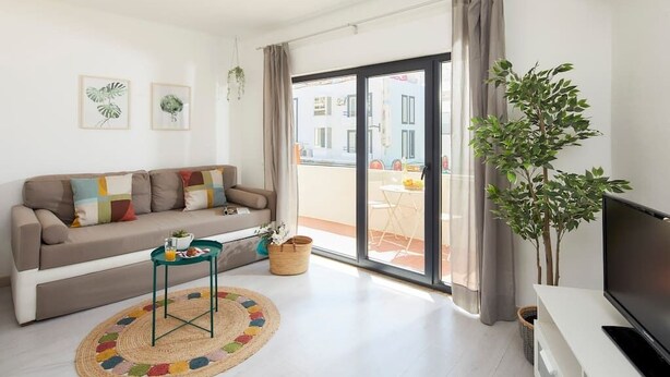 A modern living room with a sofa, a coffee table, a TV, and a balcony with a plant.