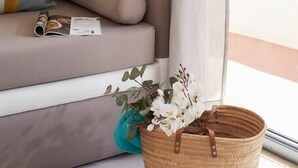 A modern living room with a sofa, a woven basket with flowers, and a window with curtains.