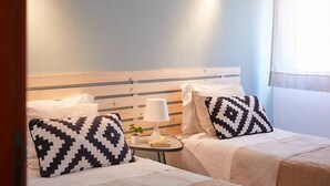 A hotel room with two beds, each with a patterned pillow, a bedside table with a lamp, and a small plant.