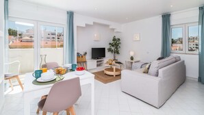A modern living room with a sofa, dining table, and TV. - ? Elegant 1-Bedroom Apartment | Pool | Walk to Old Town & Fisherman’s Beach (Albufeira)