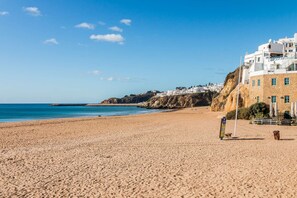Une plage avec un rivage sablonneux, un ciel bleu dégagé et des bâtiments en arrière-plan.