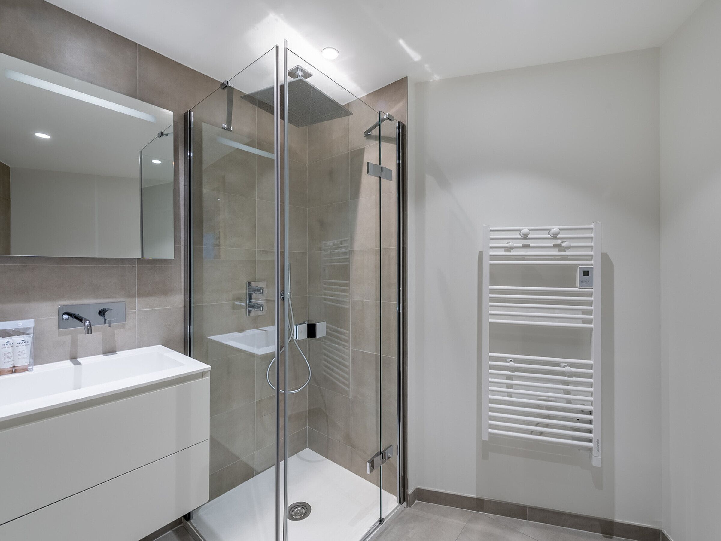A modern bathroom with a glass-enclosed shower, a white sink, and a towel rack.