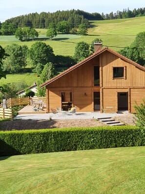 A wooden cabin with a deck, surrounded by a well-maintained lawn and a hedge. - Quiet family chalet "1083" near Gérardmer sauna (Gerbépal)