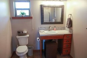 A compact bathroom with a toilet, sink, mirror, and a small window with a plant.