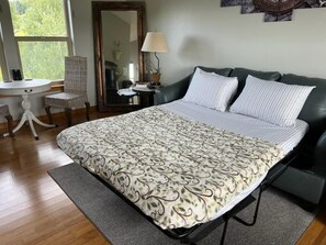 A bedroom with a bed, a desk, a chair, a mirror, and a window.