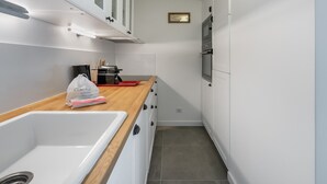 Una cocina estrecha con armarios blancos, encimera de madera, un lavamanos, una cafetera y un refrigerador.