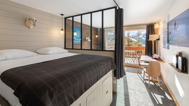 Un dormitorio con cama, escritorio y silla. Se ve un ventanal con vistas al exterior.