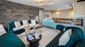 Una sala de estar moderna con una pared de piedra, sofás verdes, una mesa de centro con libros y una zona de comedor con una mesa y sillas de madera.