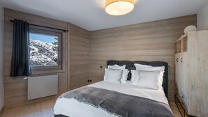 Un dormitorio con una cama grande, paredes de madera, una ventana con vista a un paisaje nevado y una lámpara en el techo.