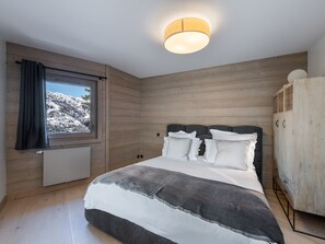 Quarto com cama grande, paredes de madeira, janela com vista para uma paisagem nevada e luminária no teto.