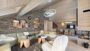 Un salon chaleureux avec un mur en pierre, des poutres apparentes en bois au plafond et un coin repas agrémenté d’une cheminée.