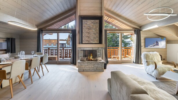 Un vaste espace de vie doté d’une cheminée, d’un plafond en bois et d’un balcon offrant une vue sur l’extérieur.