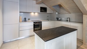 Une cuisine moderne avec des meubles blancs, un four encastré et un îlot central doté d’un plan de travail foncé.