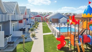 Un complexe hôtelier doté d’une allée centrale, d’un espace extérieur aménagé avec des sièges, d’une piscine et d’une aire de jeux pour enfants.