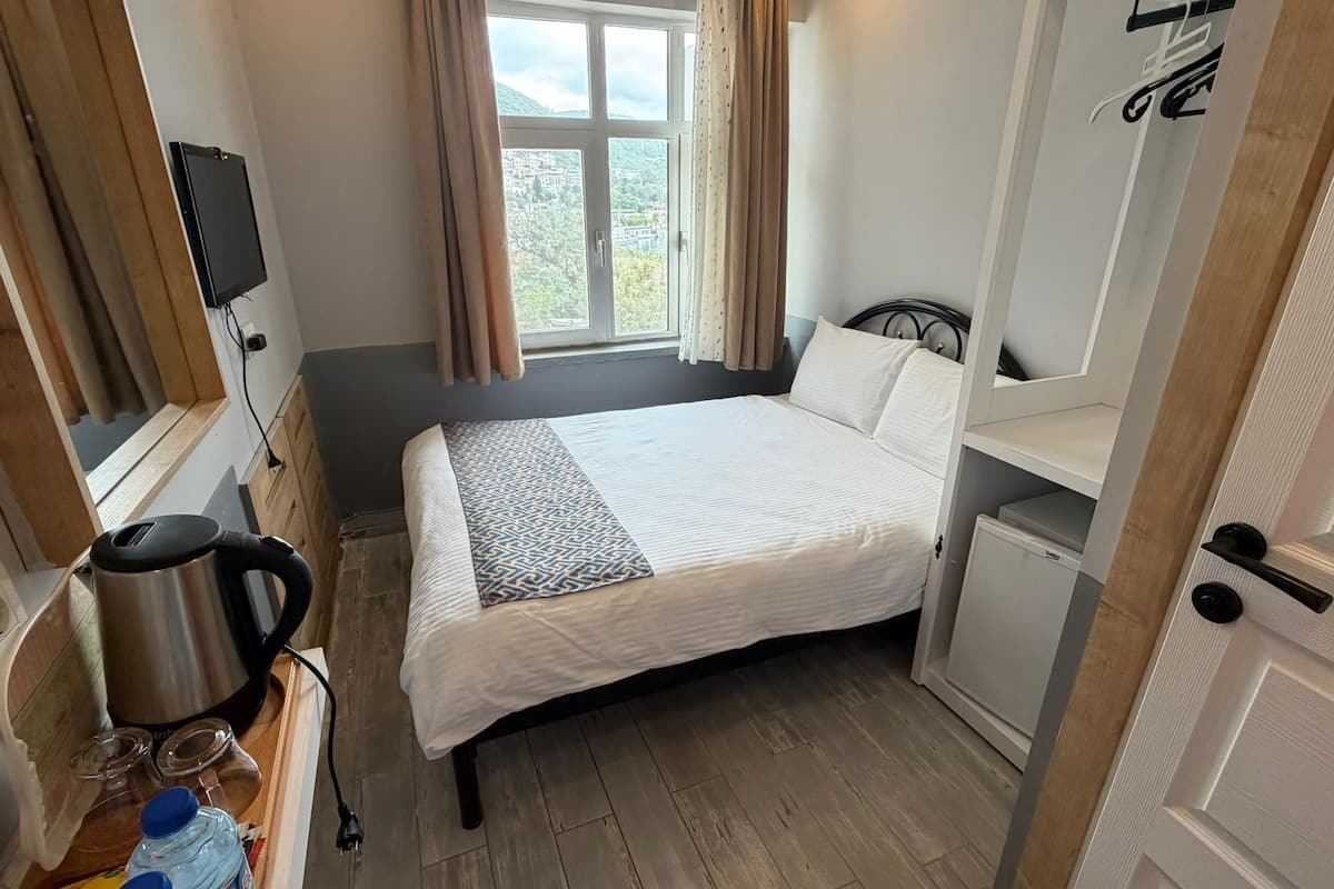 Un dormitorio compacto con cama, escritorio, silla, televisor y ventana con cortinas.