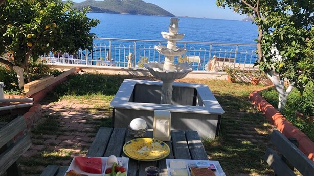 A picnic setup with a table, food, and a fountain in a scenic outdoor area with a view of the sea. - Yalı Pansiyon (Kas)