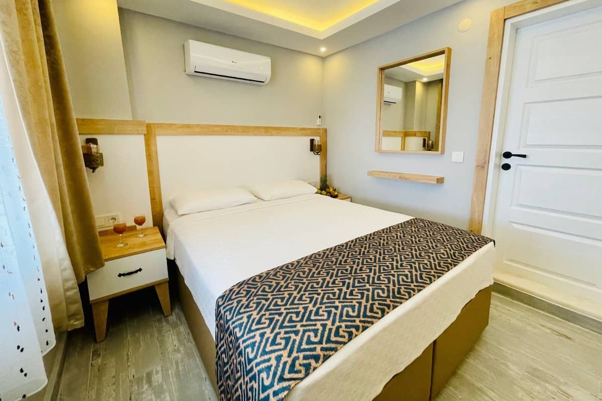 Habitación de hotel con cama, mesita de noche, espejo y aire acondicionado.