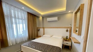 A modern hotel room with a large bed, a nightstand, a mirror, and an air conditioning unit on the wall. - Yalı Pansiyon (Kas)