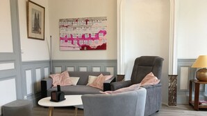 Un salon moderne avec un canapé gris, un fauteuil gris, une petite table blanche et un élément décoratif mural.