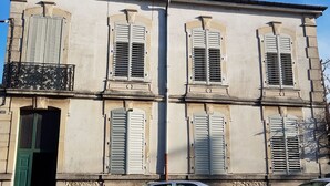 Un bâtiment doté de trois fenêtres, chacune avec des volets, et d’une porte verte.