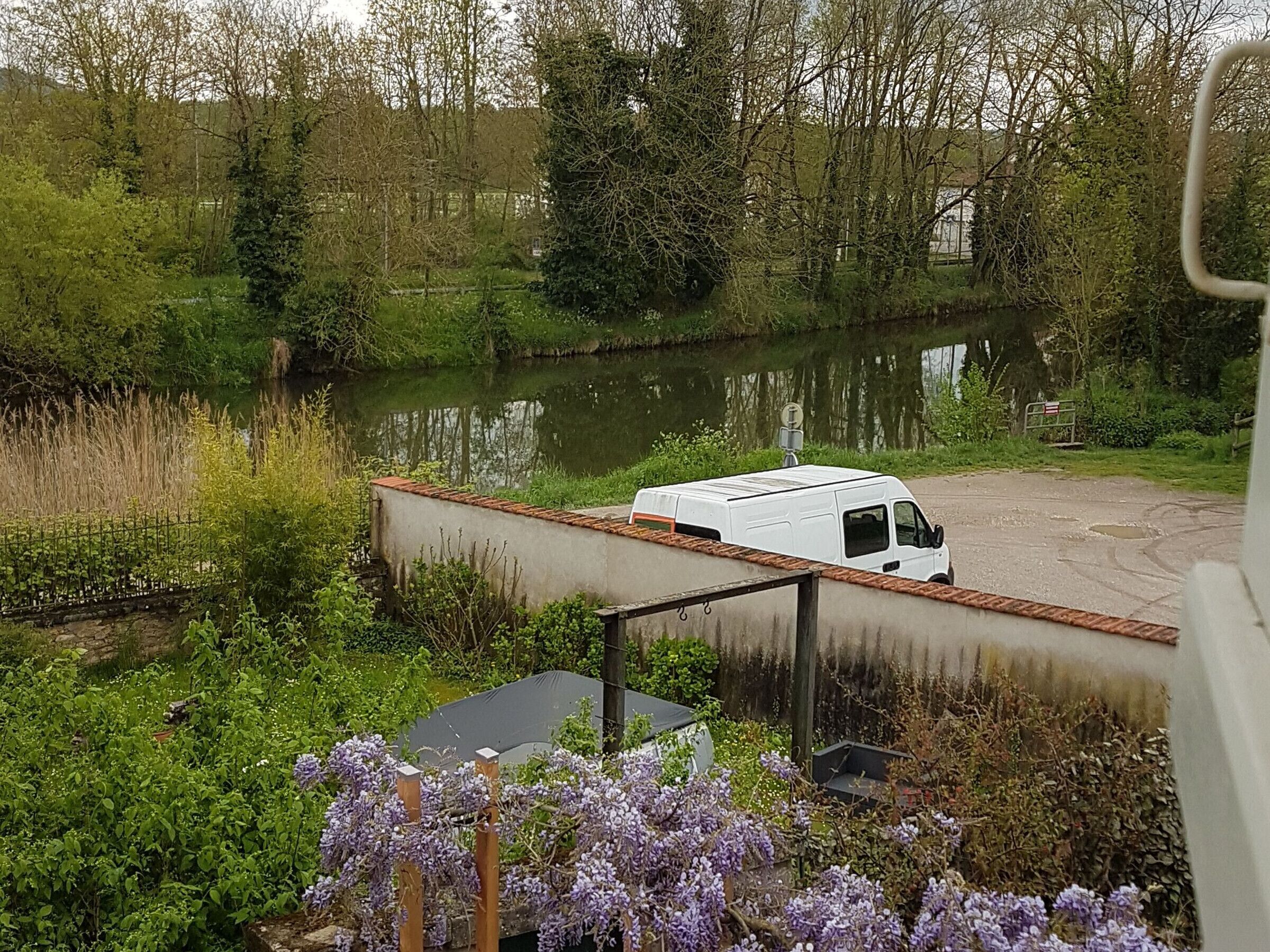 A white van parked near a river with a concrete structure and greenery.