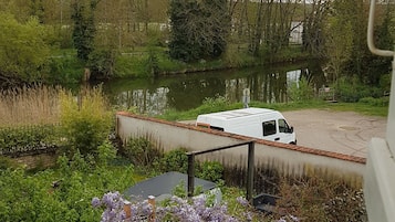 Een witte bus geparkeerd in de buurt van een rivier met een betonnen constructie en begroeiing.