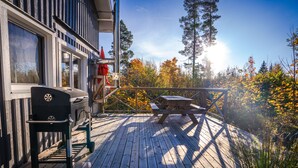 A wooden deck with a barbecue grill, picnic table, and a view of autumn foliage. - Sunny Swedish cottage surrounded by forest & tranquillity (Åsensbruk)