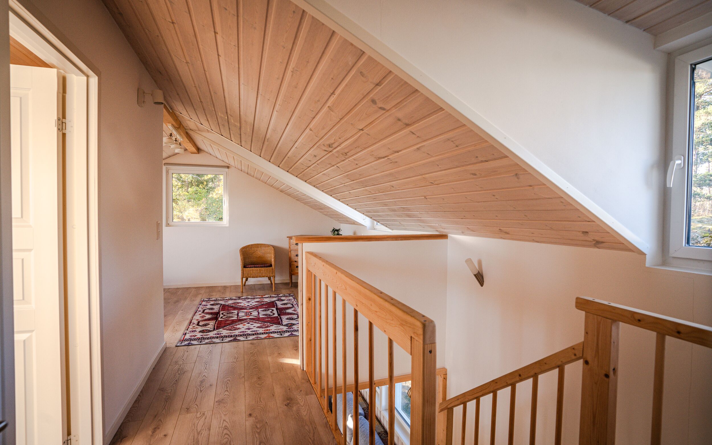 A wooden staircase leading to an upper floor with a sloped ceiling, a small window, and a patterned rug on the floor.
