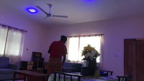 A living room with a ceiling fan, a table with a floral tablecloth, and a window with curtains. - 25 minutes to Winneba Beach!!  A quiet family suite with dining and living area. (Winneba)