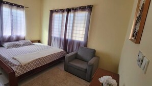A bedroom with a bed, a chair, a nightstand, and a window with curtains. - 25 minutes to Winneba Beach!!  A quiet family suite with dining and living area. (Winneba)