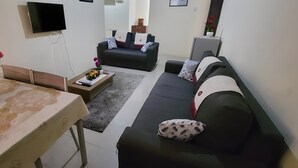 A modern living room with a sofa, a coffee table, a TV, and a vase with flowers. - 25 minutes to Winneba Beach!!  A quiet family suite with dining and living area. (Winneba)