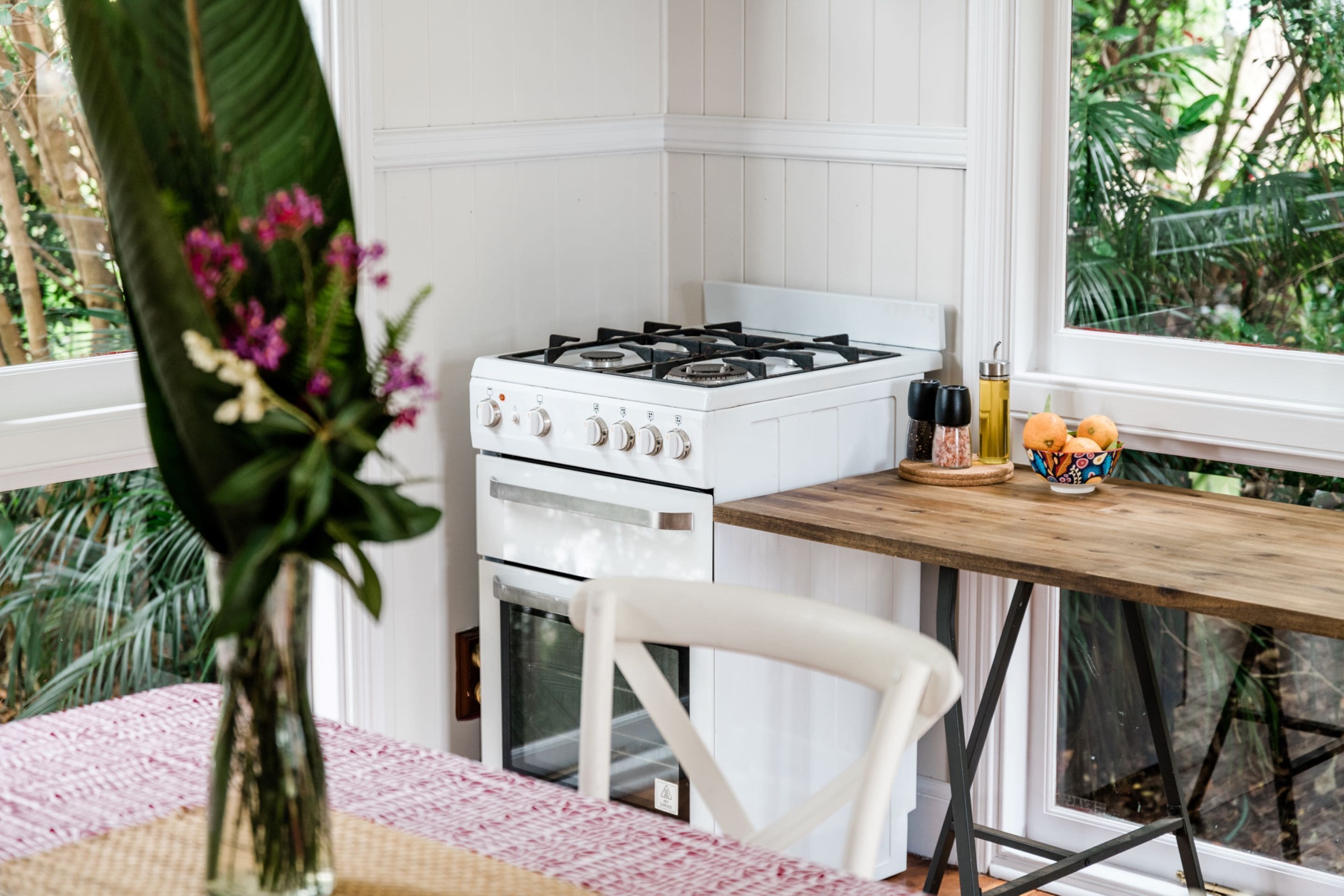 A kitchen with a white stove, a wooden table, and a window with a view of greenery.