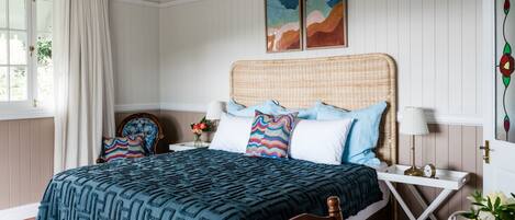 A bedroom with a bed, nightstands, a chair, a window with curtains, and wall art.