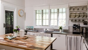 Una cocina con una mesa de madera, armarios blancos, un fregadero y una ventana con persianas.