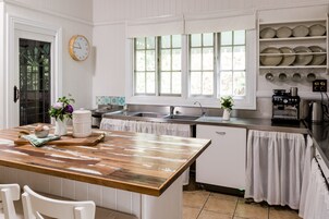 Una cocina con una mesa de madera, armarios blancos, un fregadero y una ventana con persianas.