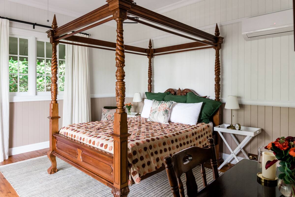 Un lit à baldaquin avec une couvre-lit à motifs floraux, une table de chevet avec une lampe et un vase rempli de fleurs.