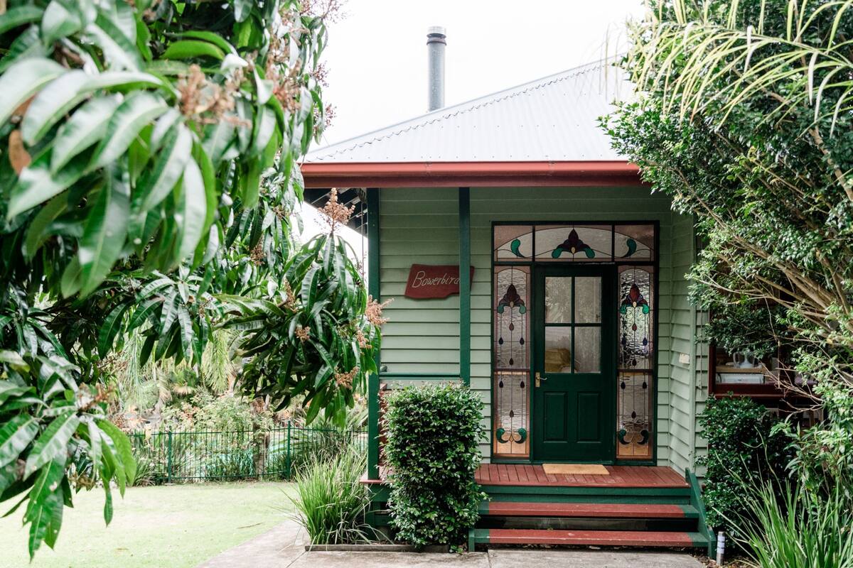 Une maison verte avec un toit rouge, une porte d’entrée dotée de panneaux de verre et une enseigne sur laquelle on peut lire « Bowerbird ».