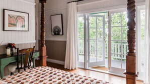 Una habitación con una cama, un escritorio y una silla. Se ve follaje verde a través de la ventana.