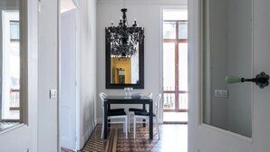 Un coin repas avec une table noire et des chaises blanches, un lustre et un grand miroir au mur.