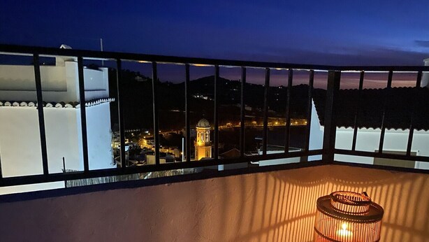 Un balcón con vistas a un paisaje urbano al atardecer, destacando un edificio con cúpula y una torre iluminada.