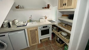 Una cocina funcional con lavadora, tostadora y estantes con vajilla y cestas.